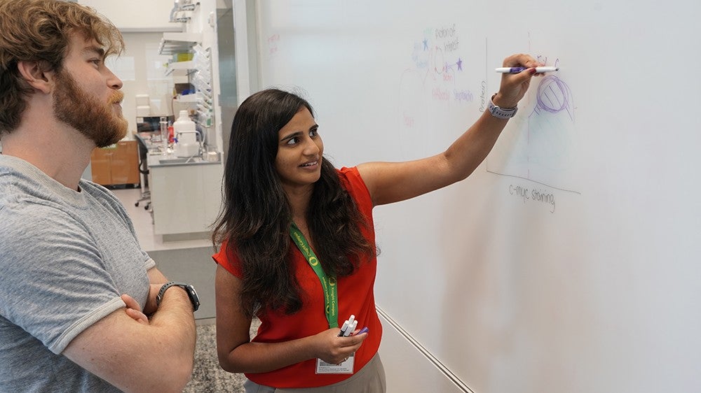 Marian Hettiaratchi writing on a whiteboard in front of a student