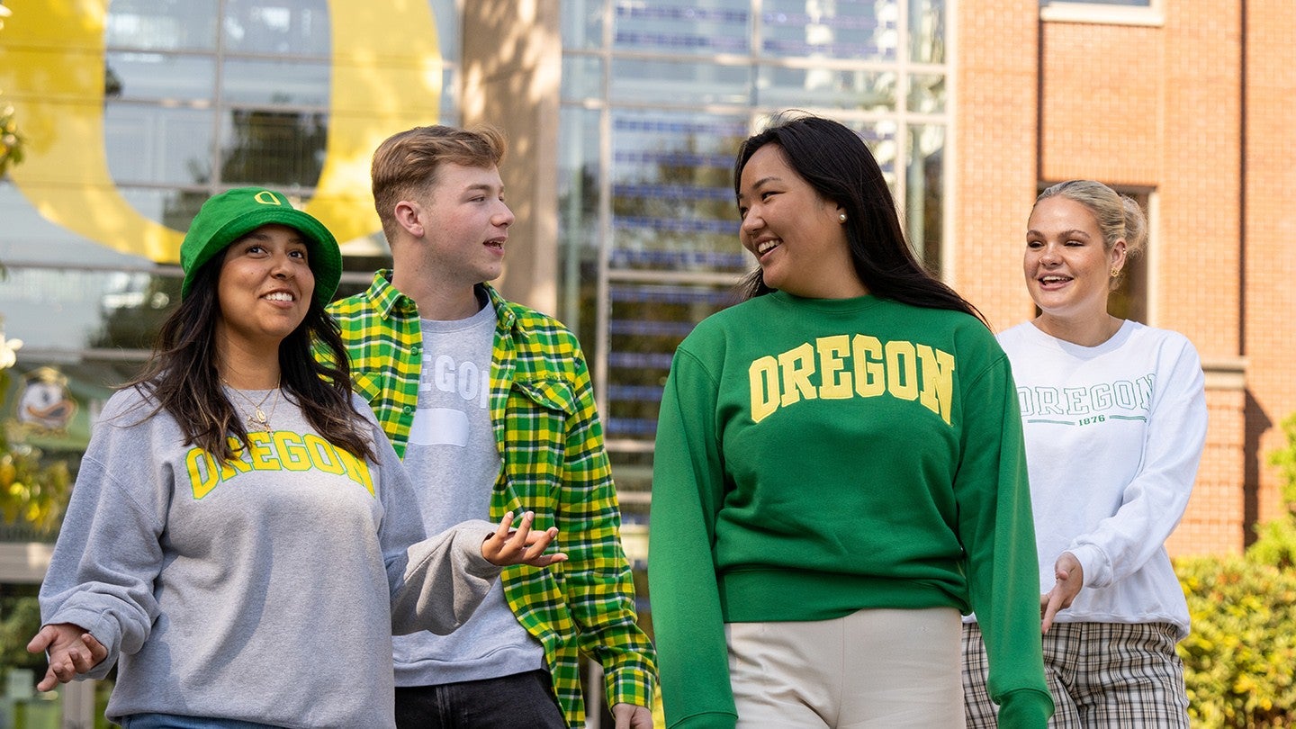 One male and three female students laughing while walking in front of the Business School on the UO campus