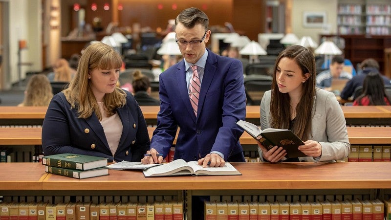 Two female, one male law student leaders consulting reference books in the law library.