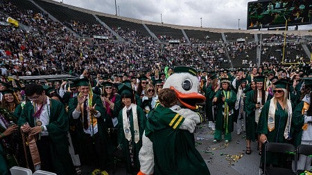 The Oregon Duck hugs a graduating senior in Autzen Stadium as thousands in caps and gowns look on