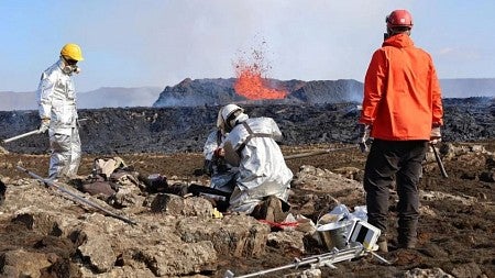 Scientists wearing protective gear collecting volcanic rock during the July 2023 Fagradalsfjall eruption.
