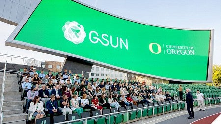 Attendees of the inaugural GSUN summit seated at Hayward Field; in the background, a digital billboard screen displays the GSUN and University of Oregon logos