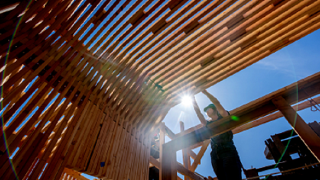 Woman wearing safety goggles framing lumber for a building's roof.