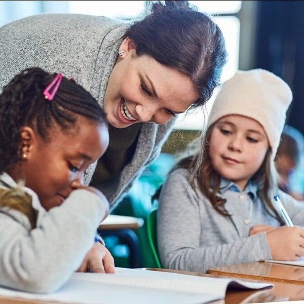 Elementary teacher helping two students with their work at desks